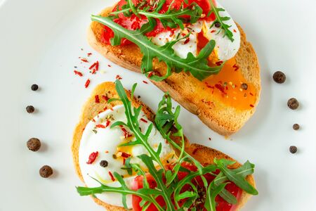 delicious poached eggs on crispy slices of wheat bread with slices of tomato, arugula, spices and...