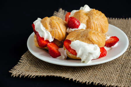 Eclairs with ice cream, whipped cream and fresh strawberries in a white plate