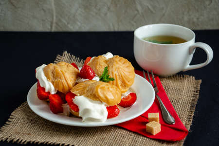 Eclairs with ice cream, whipped cream and fresh strawberries with a cup of green tea