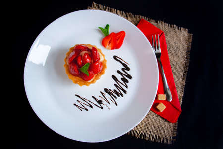 Appetizing strawberry tartlet glazed with clear jelly, on a white plate with chocolate icing