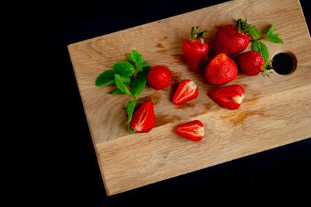 Appetizing juicy bright strawberries on a kitchen wood board on a black background with branches of...
