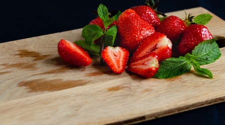 Appetizing juicy bright strawberries on a kitchen wood board on a black background with branches of fresh mintの写真素材