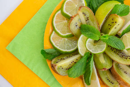 beautiful slicing of juicy fresh fruits - lime, kiwi, decorated with a sprig of mint on a yellow and green napkinの写真素材
