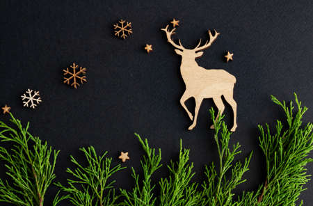 Stylish christmas composition on a black background, wooden figurines of deer, snowflakes and fir...