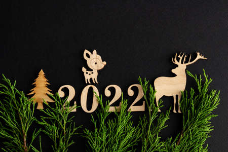 2022, Stylish christmas composition on a black background, wooden figurines of deer and fir...