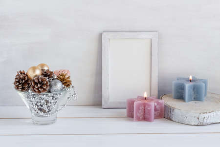 Christmas decoration, mock up in a white frame with a composition of cones and new year beads, candles on a white table, copy space. High quality photoの写真素材