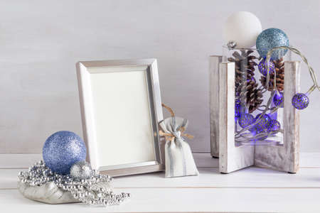 Christmas decoration, white frame mockup, christmas balls and blue garland on a white table, copy...