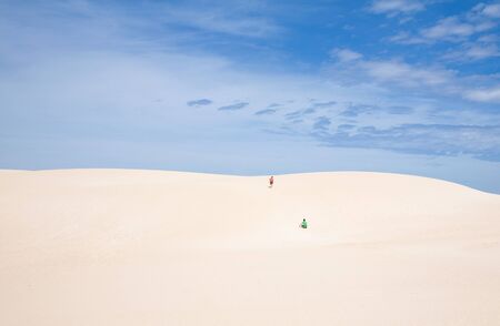walking in dunes - two boys in red and green t-shirts and shorts walking uphill in the dunes of Corralejo, Fuerteventura, Canary Islands, Spainの写真素材