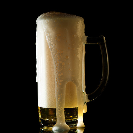 overflowing beer mug isolated on blackの写真素材