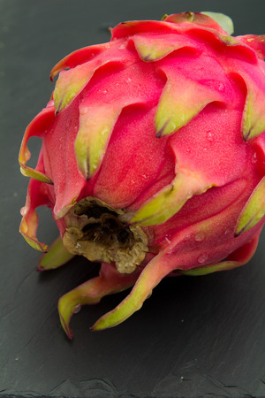 whole red dragon fruit with green scaleson black slate sufraceの写真素材