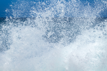 sea water foam flying against the backdrop of blue waterの写真素材