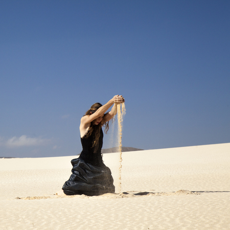 young attractive woman in black flamenco dress playing with the sand in dunesの写真素材