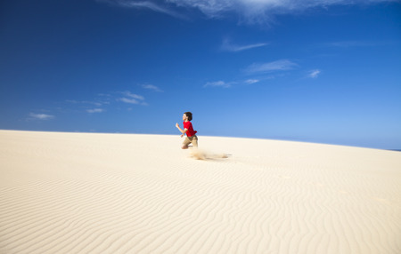 Fuerteventura sand dunes in the north of the island, teenage boy in red t-shirt and shorts running in a silly manner, fooling aroundの写真素材