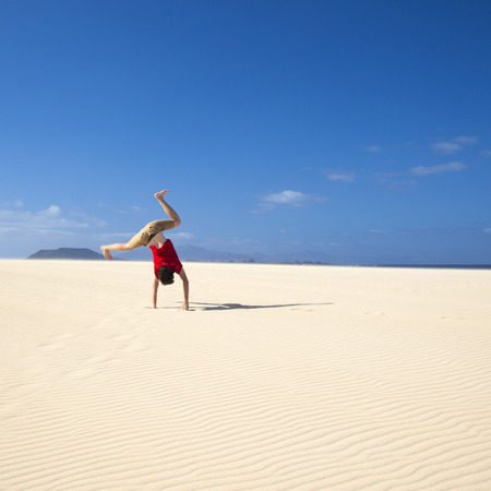 Fuerteventura sand dunes in the north of the island, teenage boy in red t-shirt making handstandsの写真素材