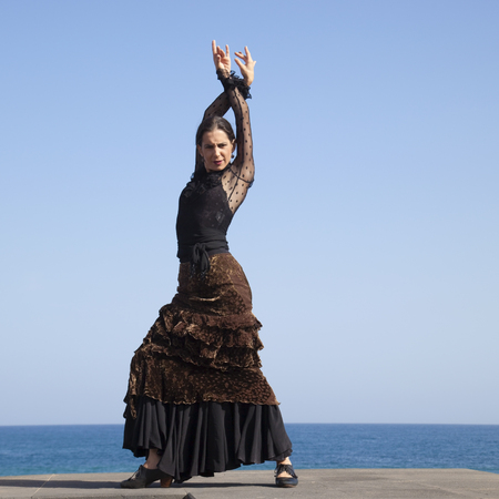 flamenco by ocean shore - young attractive woman in a long blac dress dances, ocean and blue sky in the backgroundの写真素材