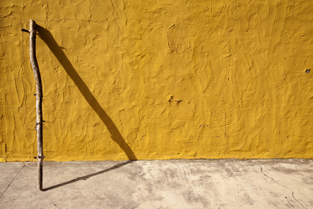 abstract background with yellow painted wall, stick and its shadow forming a triangleの写真素材