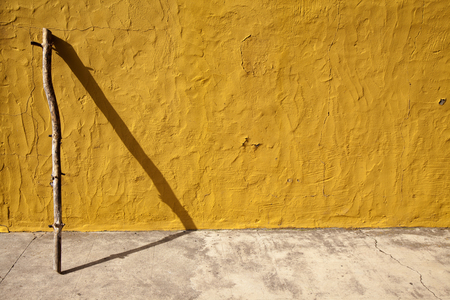 abstract background with yellow painted wall, stick and its shadow forming a triangle