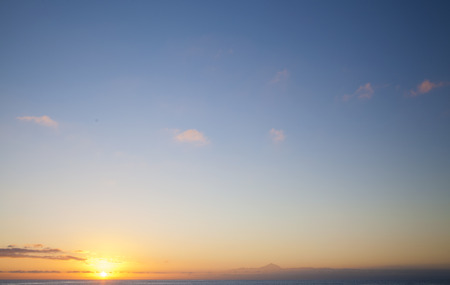 Sunset over Atlantic ocean as seen from Puerto de Las Nieves on Gran Canaria, natural background of predominantly sky, peak of Teide on Tenerife on the lower edge of the picture, light pink cloudsの写真素材