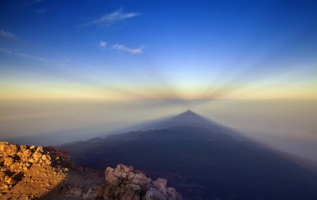 Sunrise on Teide, the tallest mountain of Spain and Atlantic Basin, view west towards  shadow of volcano cast onto the morning mist, lower levels of Tenerife visible, anticrepuscular rays in the skyの写真素材