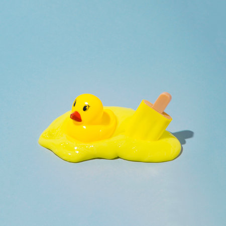 Melted yellow ice cream with yellow duck. On a blue background. Minimal composition.の写真素材