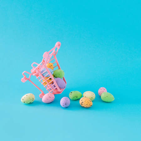 Easter eggs falling out of a pink shopping cart. On thegently blue background. Minimal composition.