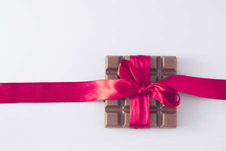 chocolate wrapped in a red ribbon in a bow. White background. Minimal composition.の写真素材