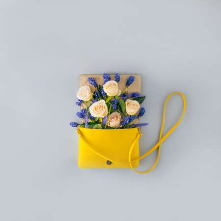 Flowering from a yellow women's bag. Spring flowers blooming from the bag. On a gray background.