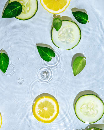 Cucumbers and lemon in water. Summer scene. Squeezing the juice. Minimal composition.