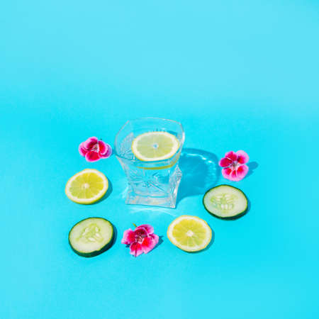Lemons and cucumbers with a glass of water and flowers around. Blue background.の写真素材