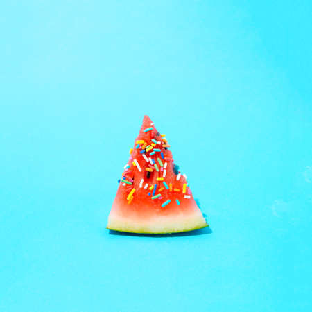 A piece of watermelon with tiny colorful candies. Summer minimal composition on a blue background.の写真素材