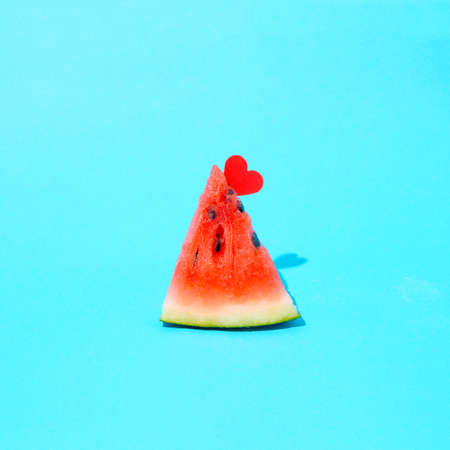 A piece of watermelon with a red heart. Summer composition on a blue background.