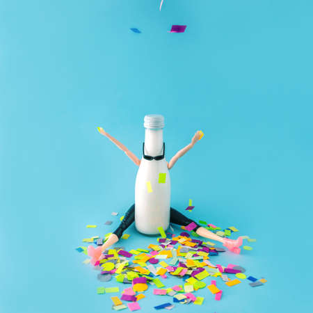 A person throwing confetti behind a white bottle with sunglasses. Celebration, party. Blue background. Minimal composition.の写真素材