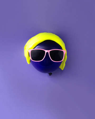 Purple balloon with yellow slime and pink glasses. Purple background. Minimalism.