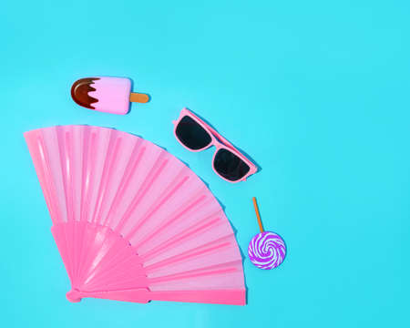 Women's accessories. Pink fan, glasses and ice cream on a summer blue background.