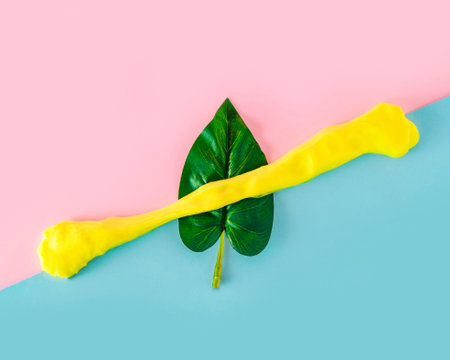 Sprinkled yellow paint on a green leaf on a blue-pink background. Minimalism.の写真素材