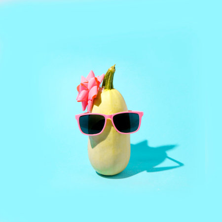 Zucchini with pink sunglasses and a pink bow. Minimal aesthetics on a blue background.の写真素材