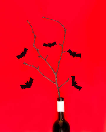 A bottle of champagne with tree branches and silhouettes of bats on a red background. Flat bed. Halloween party concept.の写真素材