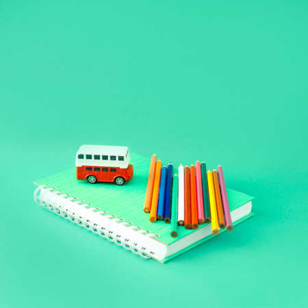 Creative look of school supplies with colorful crayons and a red bus on a pastel blue background. Minimal concept.の写真素材