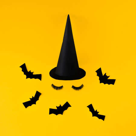 Creative witch look made of bats, hats and artificial beauty eyelashes. Minimum flat laying. Halloween concept. On a yellow background.の写真素材