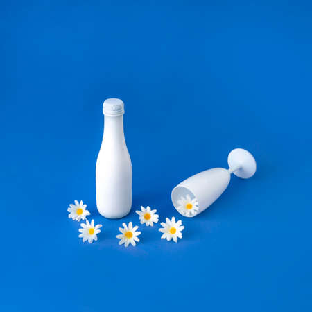 White glass and wine bottle with white flowers coming out of the glass. Creative minimal composition on a blue background.の写真素材