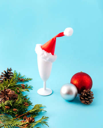 Christmas or New Year parties look great with white glass, a Santa hat, colorful Christmas decorations, green twigs and a pine cone. Light blue holiday party background.の写真素材