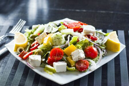 Vegetable salad on the plate, tomatoes, green salad, cheese, lemon and olive, other vegetables. on the black background.の写真素材