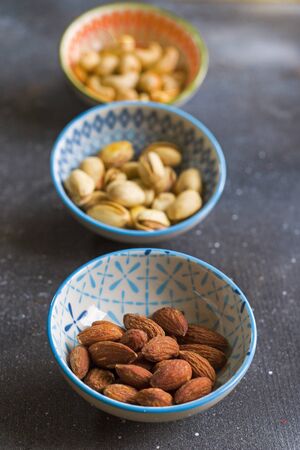 Nuts in bowls on the table, almonds, cashews and coasted nuts on the blue background. Colorful nuts set.の写真素材