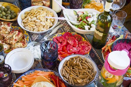 Full table view, tomatoes, snacks, wine, water with lemon and mint, salad, pizza and other food on the table for party and family eating.の写真素材