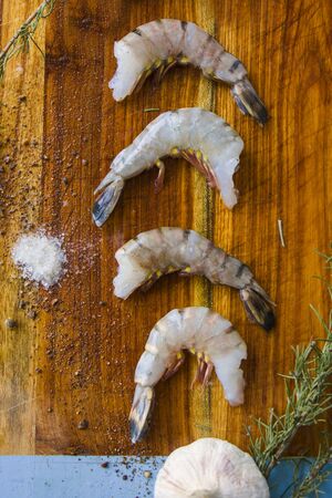 Raw shrimps on the wooden board with salt, dry pepper and rosemary, natural light.の写真素材