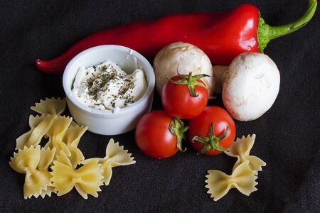Spaghetti and farfale ingredient tomatoes, mushroom fungus, red pepper and souse with spices on the black background, studio shoot.の写真素材