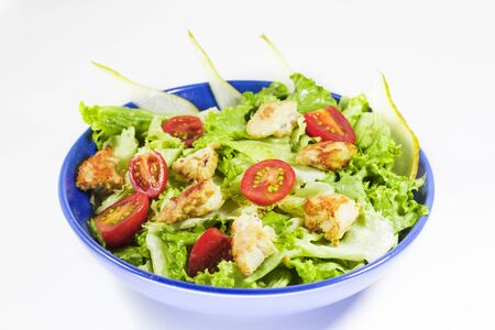 Chicken salad with tomatoes, pear and green salad on the blue bowl, white background.の写真素材