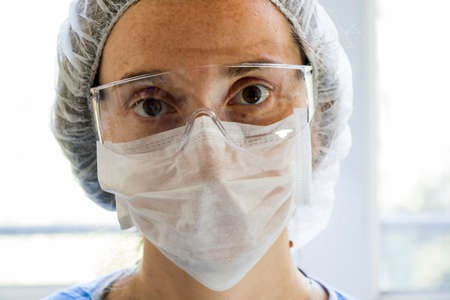 Woman doctors portrait, young girl doctors face with mask and safety glass uniform. Uniform for surgery and viruses. close-up.の写真素材