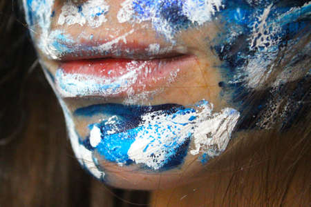 Painted face with acrylic blue and white colors. Young beautiful woman portrait, close-up photo.の写真素材