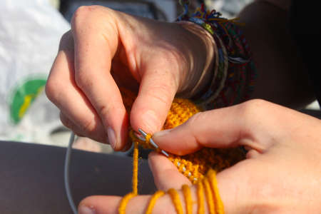 Knitting scene. Hand and knitting needles. Yellow and orange clothing. Close-up and macro.